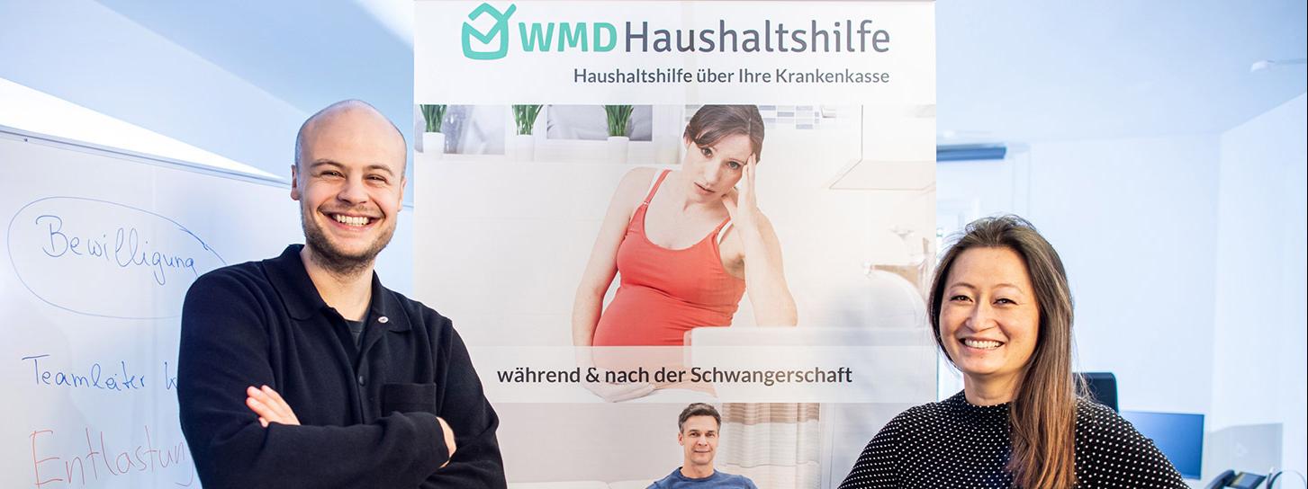 Jume Lee und Enrico Westrup in front of an marketing poster of their company