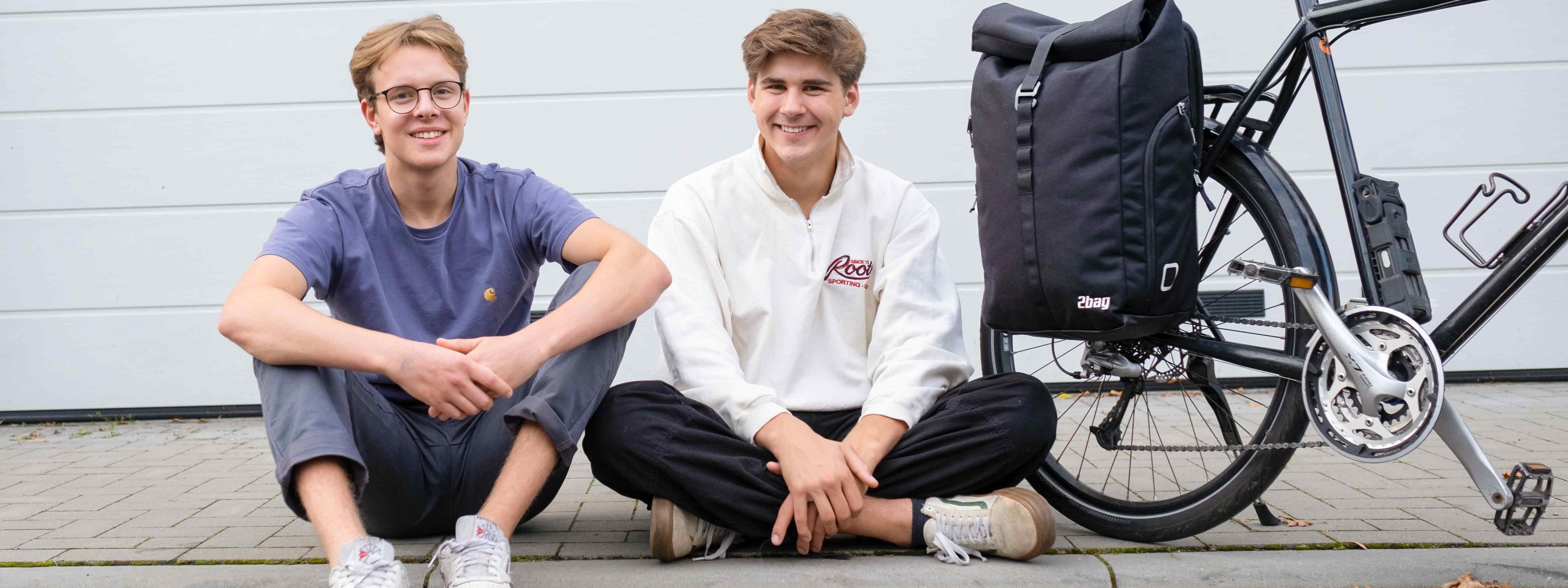 Leander Mellies und Karl Fischer vom Start-up 2bag sitzen auf dem Bordstein neben einem Fahrrad