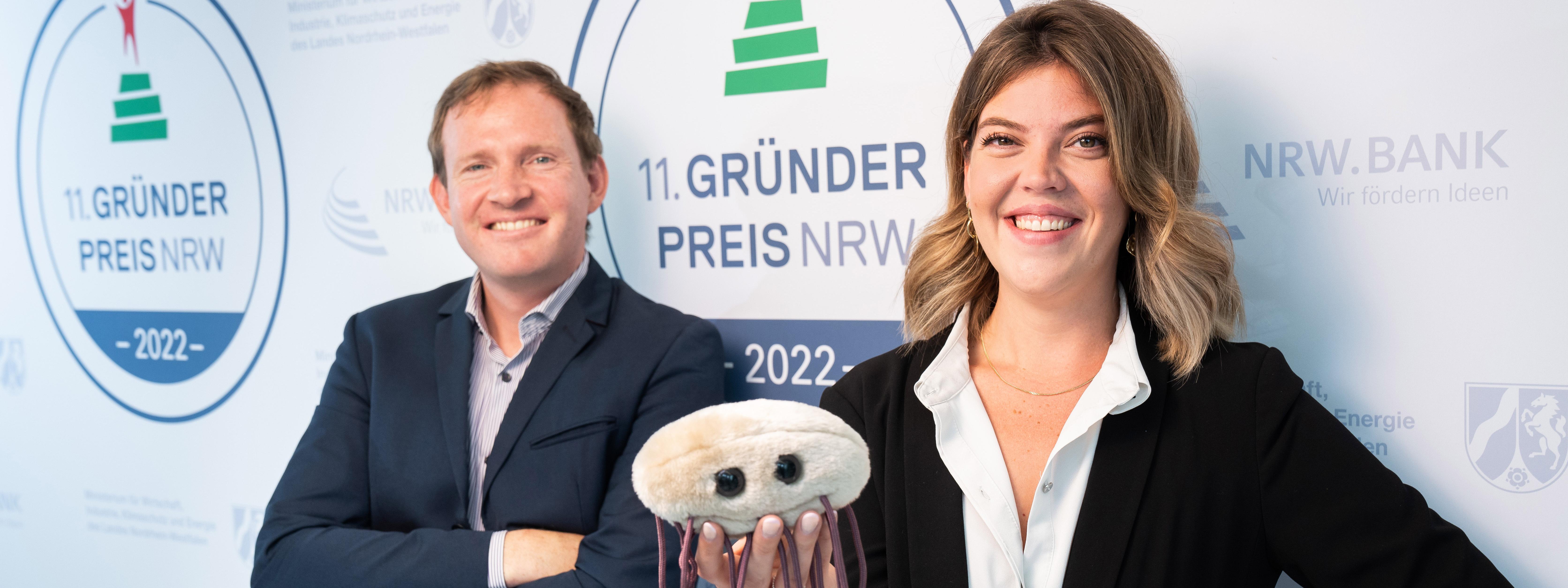 Dr. Christian Schwarz, Gründer von Numaferm, und eine Frau stehen vor dem Gründerpreis-Logo