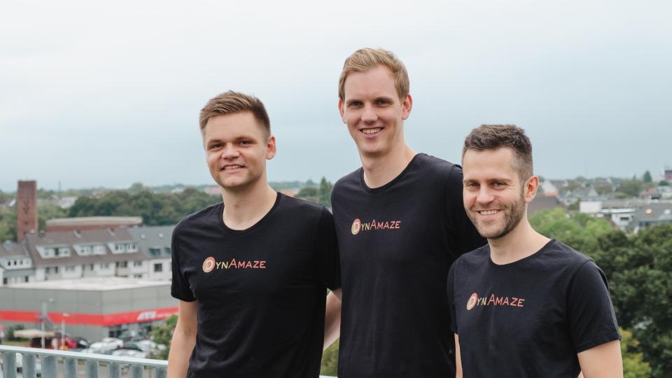 Die drei Gründer von DynAmaze stehen nebeneinander auf einer Dachterrasse