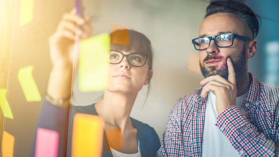 A man and a woman working with post its on a glass wall