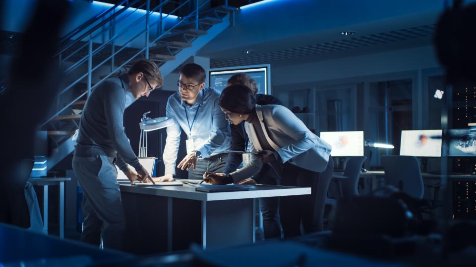 Vier Personen stehen zusammen im Büro und schauen gemeinsam auf einen Laptop